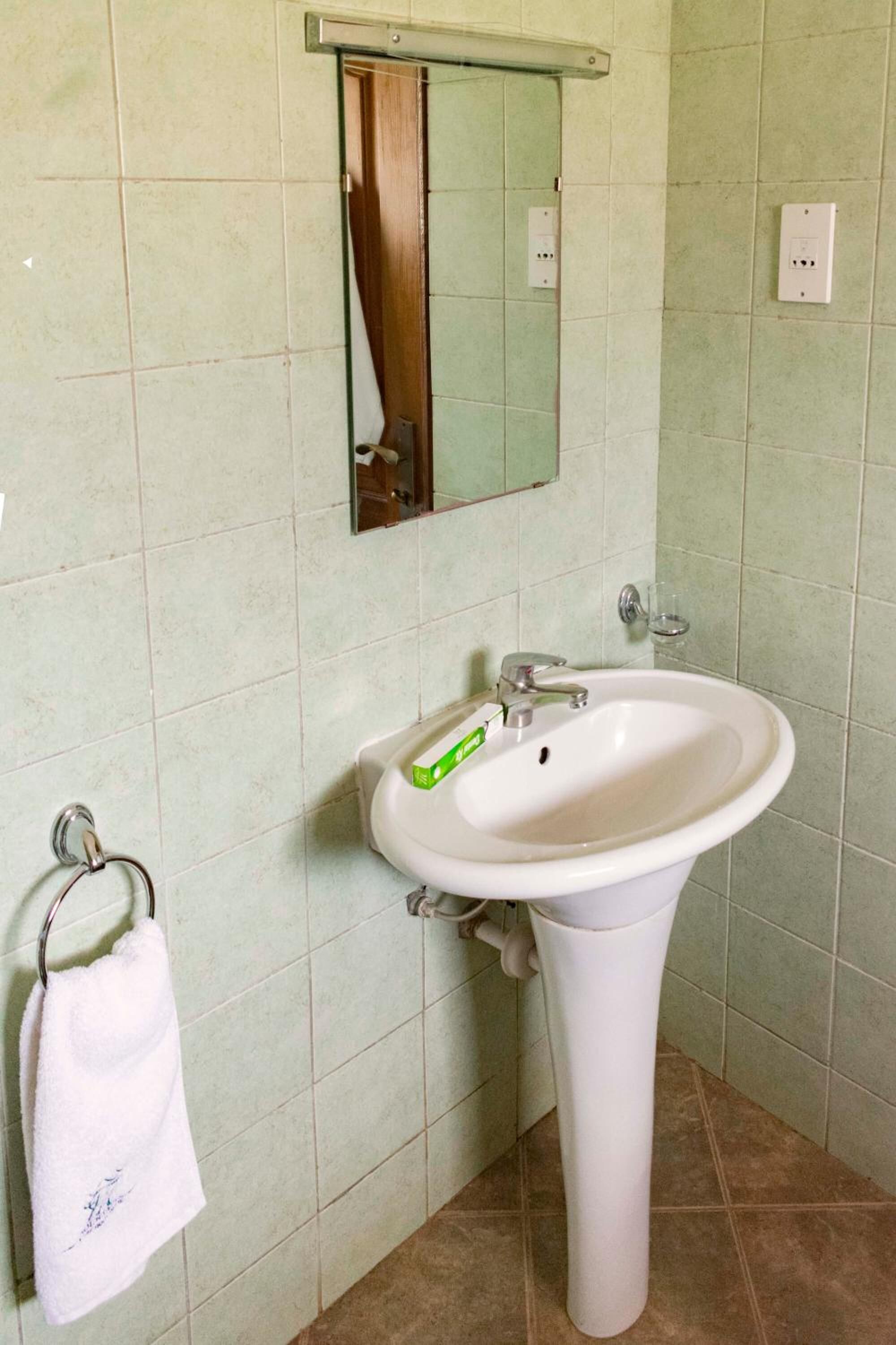 Een badkamer met een wit wastafeltje op een voet, een spiegel erboven en een handdoekrek met een witte handdoek.