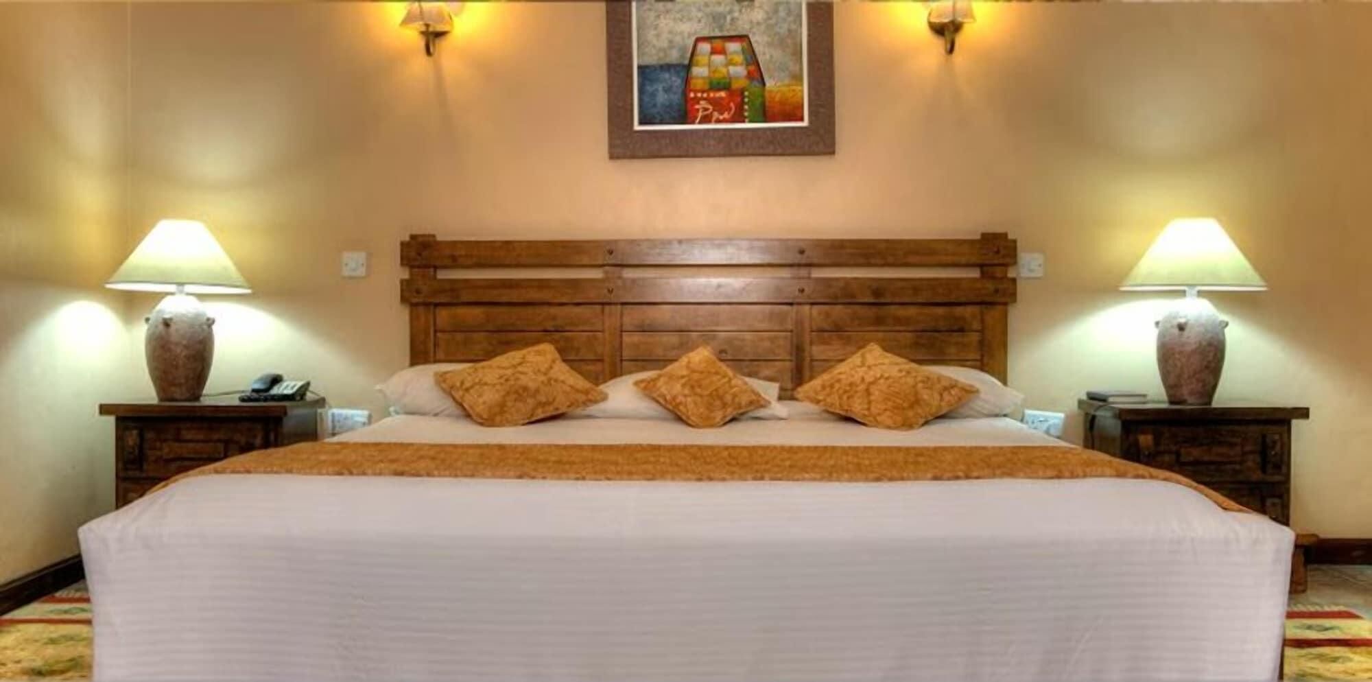 A hotel room with a wooden headboard, a large bed with white bedding, two bedside lamps, and a painting on the wall.