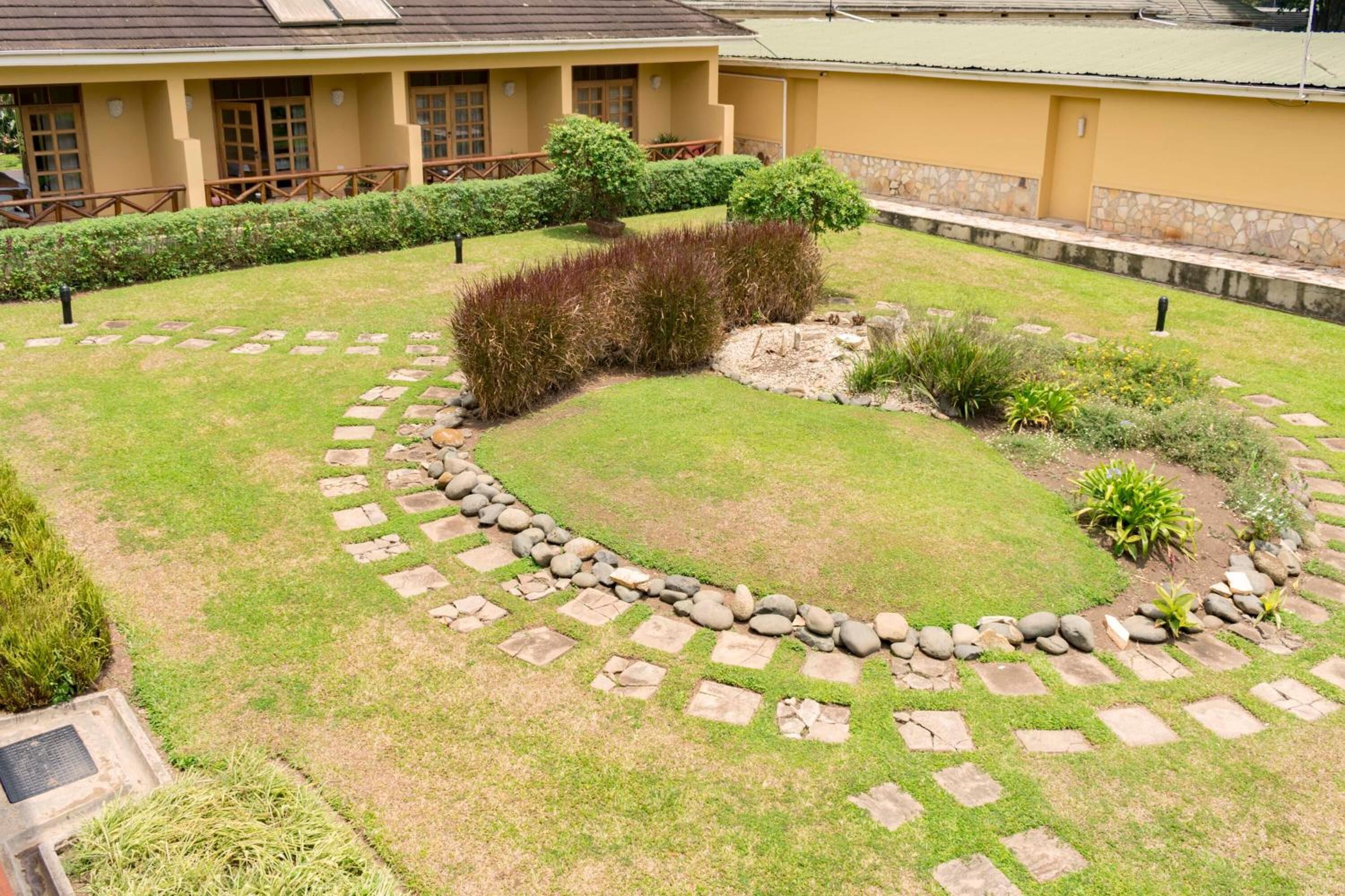 A courtyard with a stone pathway, green lawns, and a building with a yellow facade.
