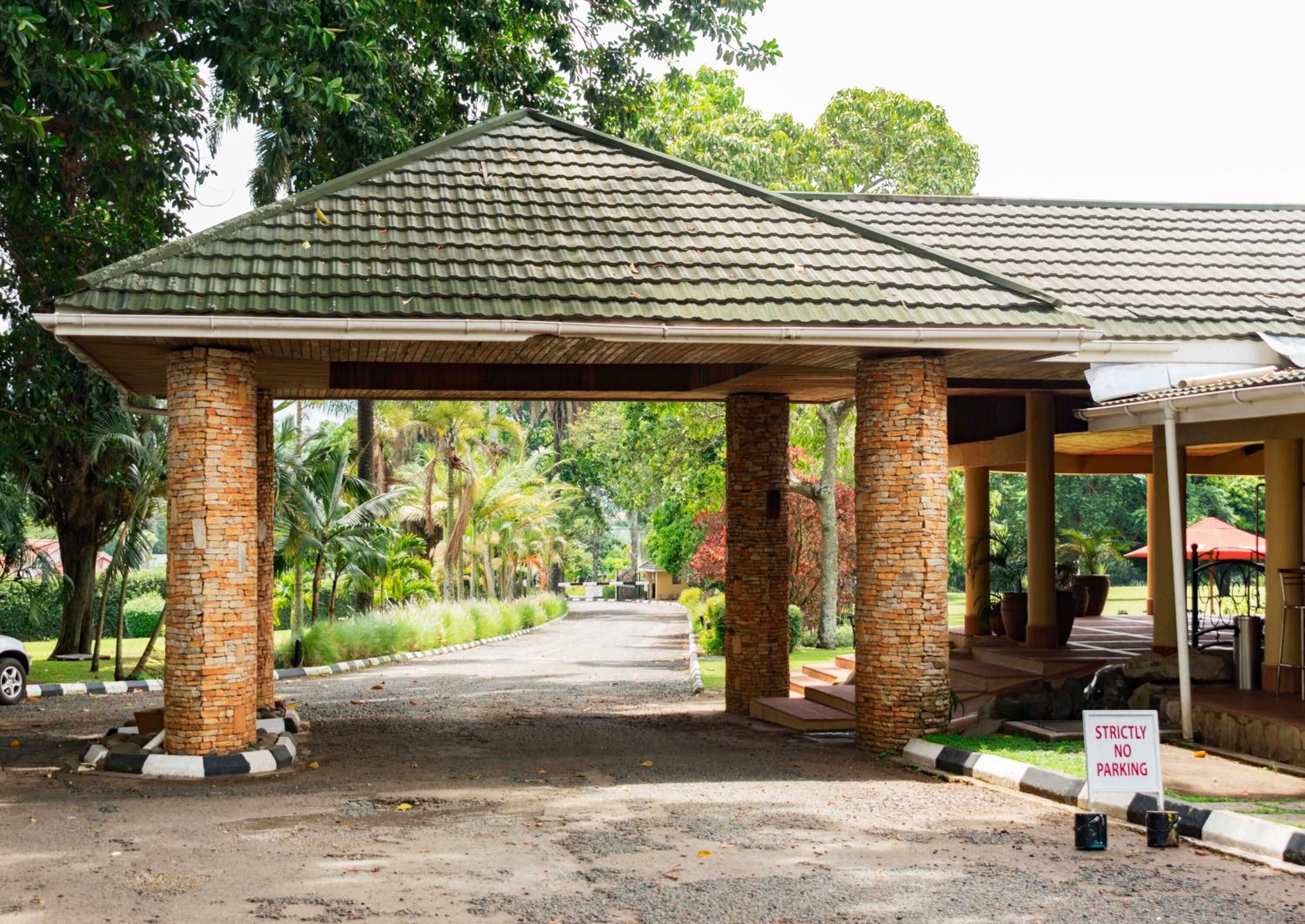 A covered pavilion with stone pillars, a gravel driveway, and a 'Strictly No Parking' sign.