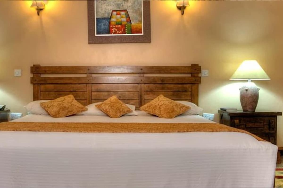 A hotel room with a wooden headboard, a large bed with white bedding, two bedside lamps, and a painting on the wall.