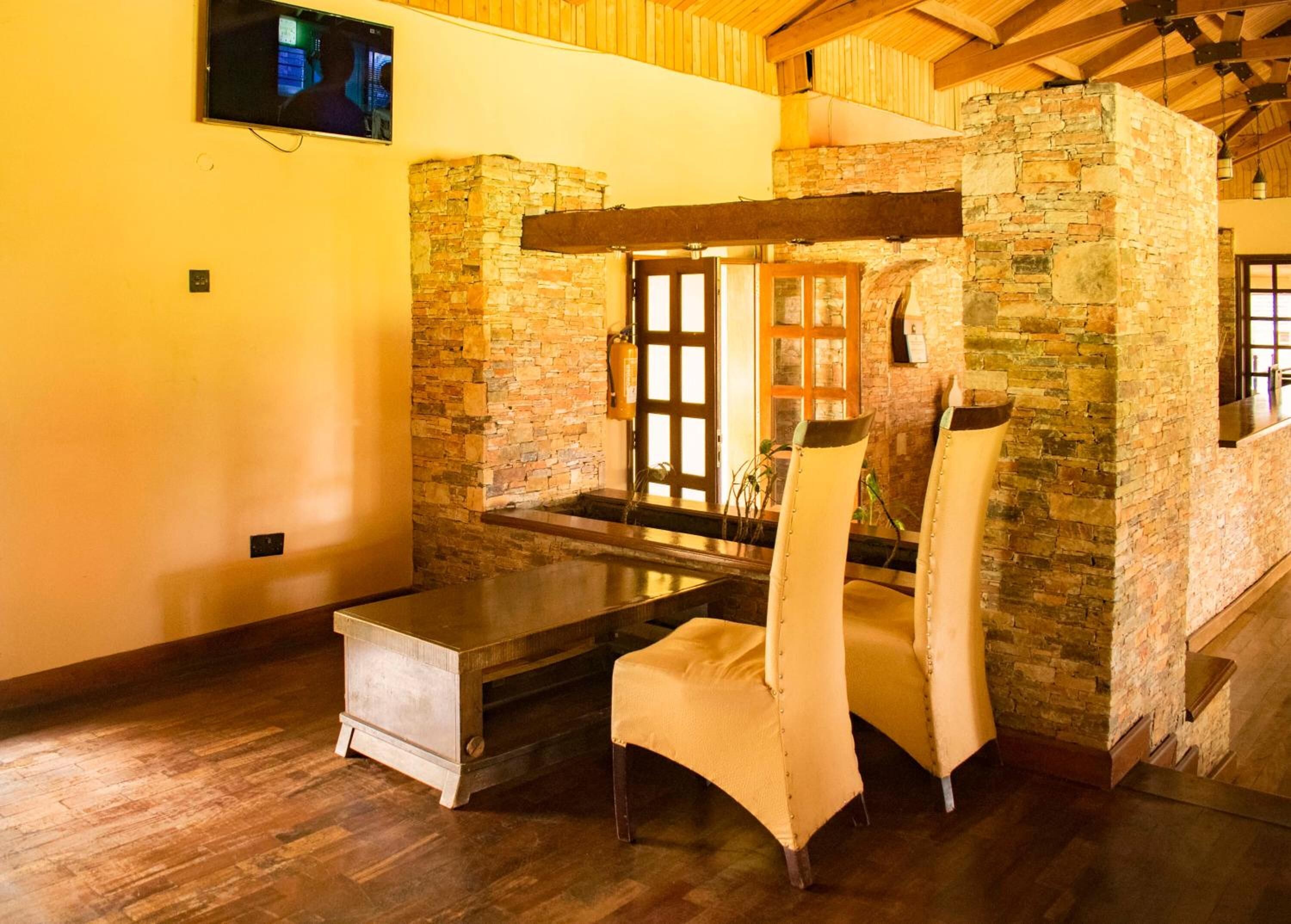 A rustic room with stone walls, wooden ceiling beams, a stone fireplace, and a television mounted on the wall.