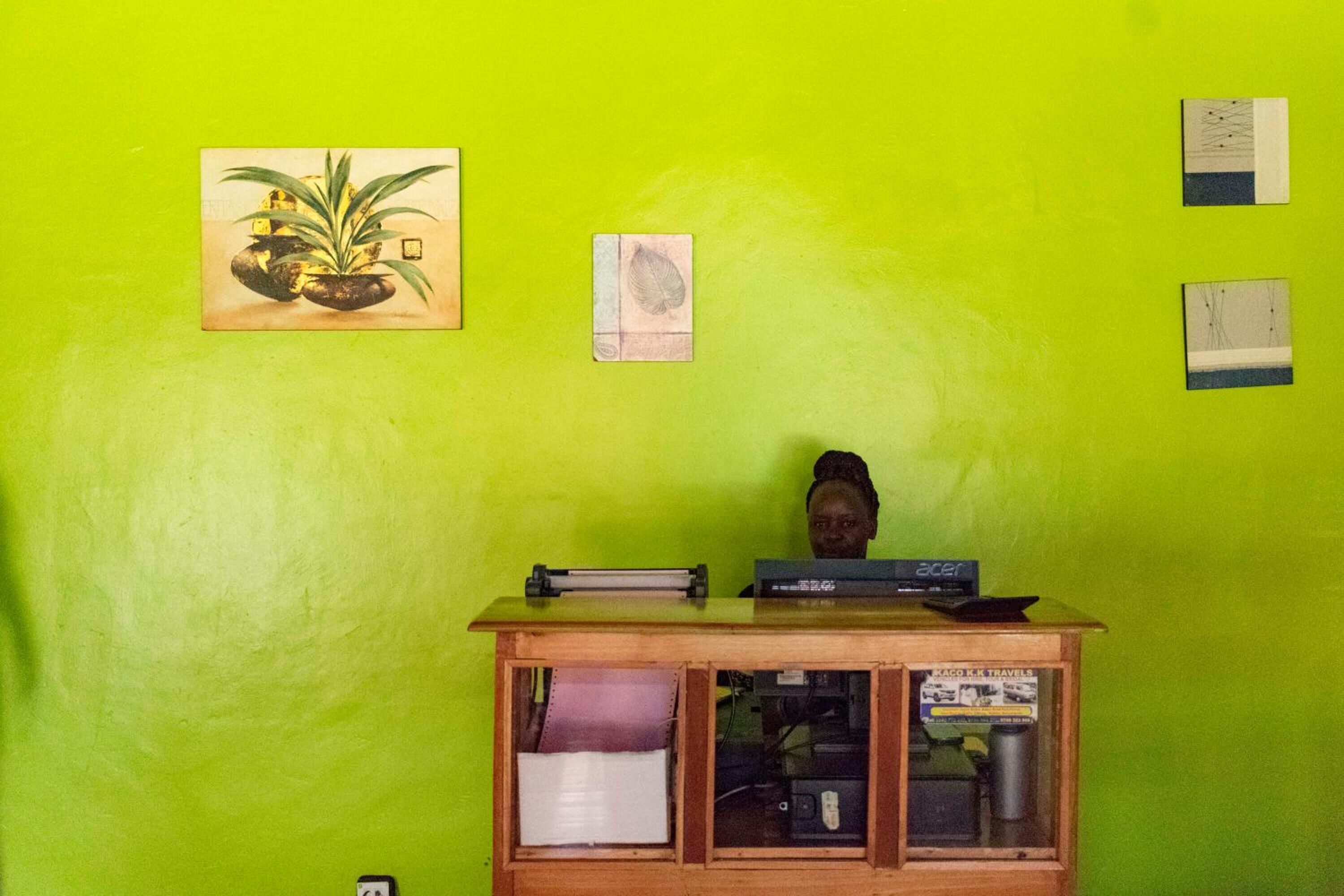 Een kamer met een heldergroene wand, een houten bureau met een computer en boeken, en ingekaderde foto's aan de muur.