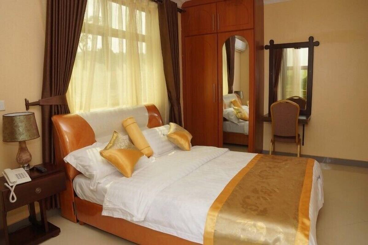 A hotel room with a bed, a nightstand with a lamp, a wardrobe, and a mirror.