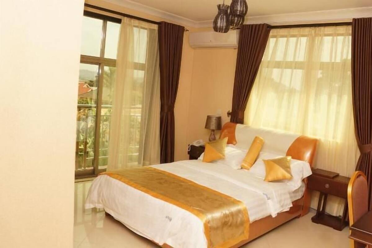 A hotel room with a large bed, a nightstand, a lamp, and a view of the outdoors.