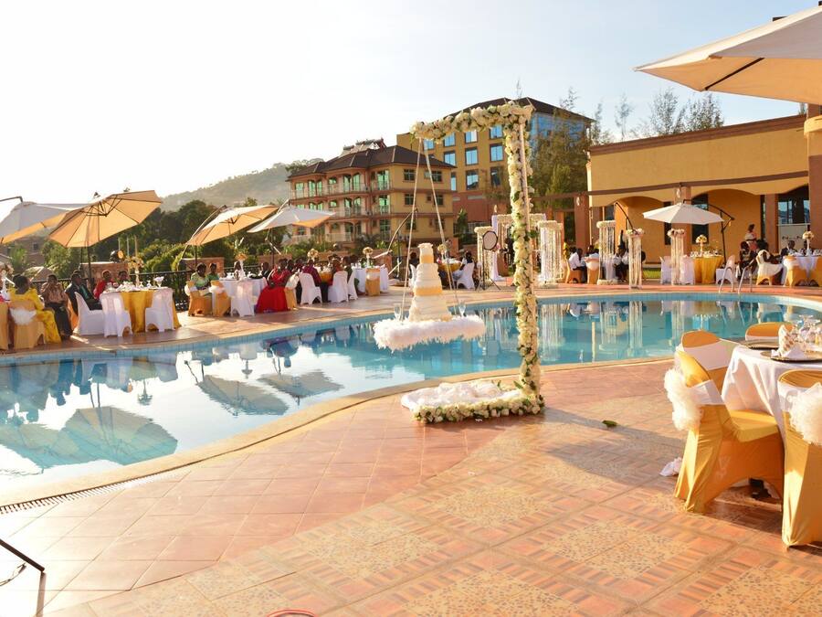 Recepción de boda junto a la piscina con mesas y sillas, un pastel de bodas de varios niveles y un edificio al fondo.