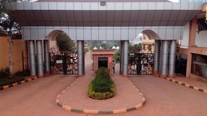 A gated entrance with a central decorative tree, flanked by metal gates with animal motifs, leading to a building with a tiled roof and a small entrance building. - Nican Resort Hotel (Kampala)