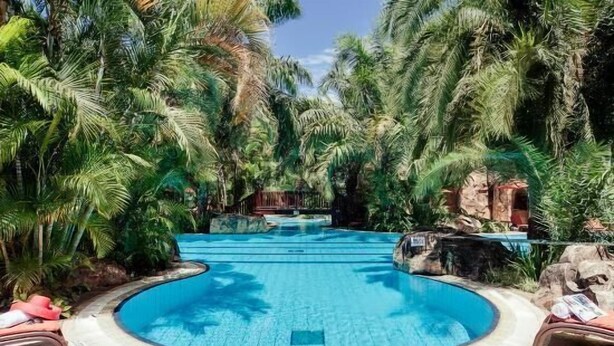 A circular pool surrounded by lush greenery and rocks, with lounge chairs and a hot tub. - Nican Resort Hotel (Kampala)