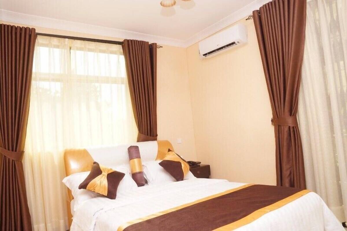 A hotel room with a bed, curtains, an air conditioning unit, and a window.