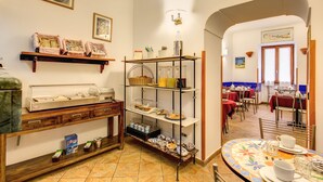 A dining area with a buffet setup, including a counter with food items and a display case. There are tables and chairs arranged for dining, and a decorative wall with framed pictures. - Hotel Gea di Vulcano (Rome)