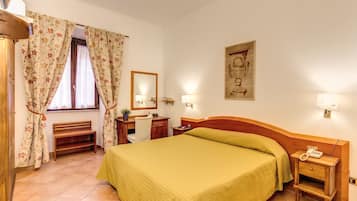 Habitación de hotel con cama, escritorio, silla, espejo, mesita de noche con teléfono y una lámpara de pared.