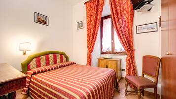 Une chambre à coucher bien rangée, avec un lit, une chaise, un bureau et un téléviseur fixé au mur.