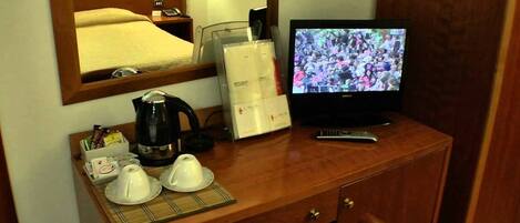 A hotel room with a wooden cabinet, a television, a coffee maker, and a tray with teapots and cups.