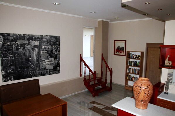 A room with a cityscape mural, a staircase, a bookshelf, and a large vase on a table. - Hotel Golden Sun (Pylos-Nestoras)