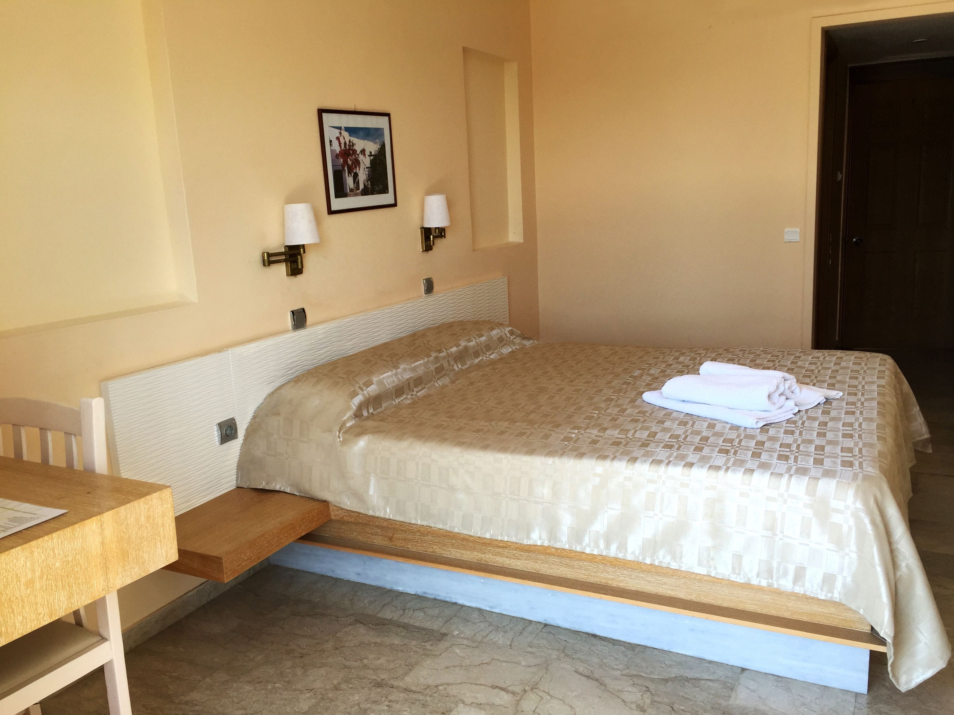 A hotel room with a bed, a desk, and a picture on the wall.