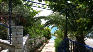 Un escalier en pierre menant à une plage offrant une vue sur la mer, entouré d’une végétation luxuriante et agrémenté d’une rambarde bleue.