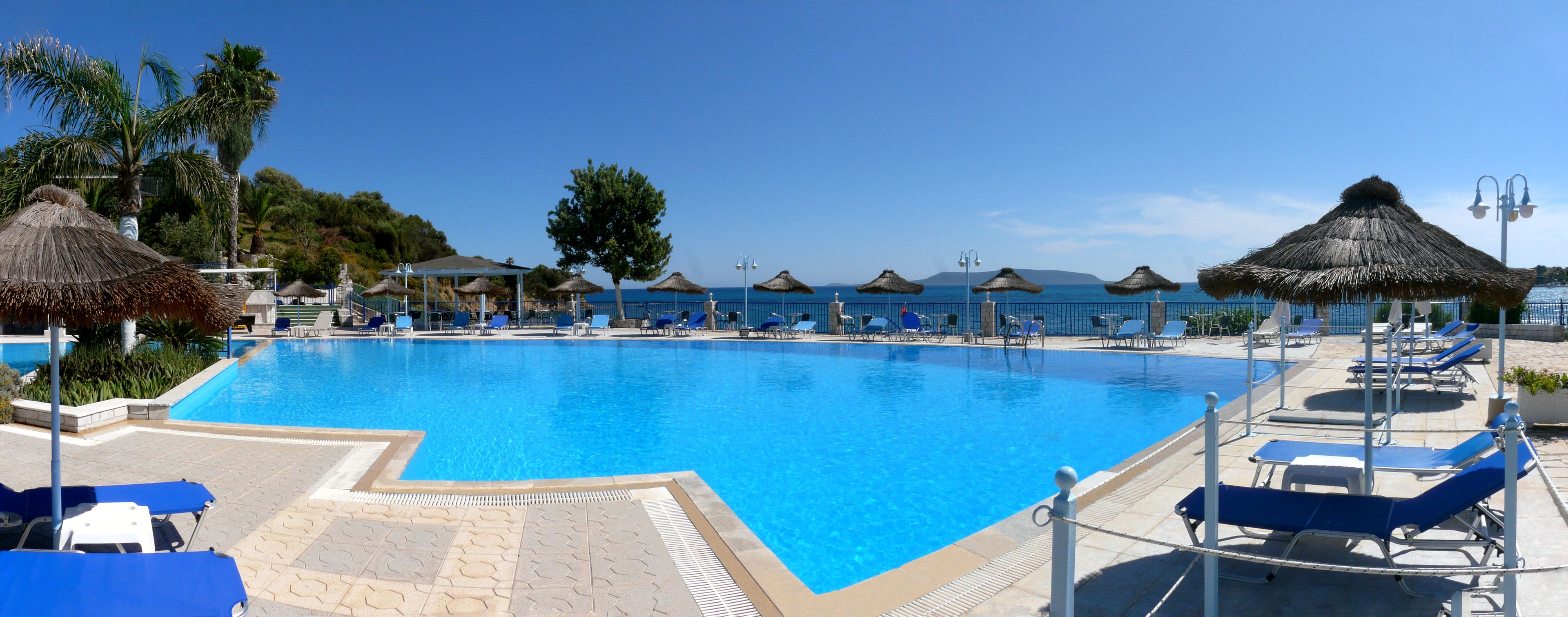 A swimming pool with blue water, surrounded by lounge chairs and thatched umbrellas.