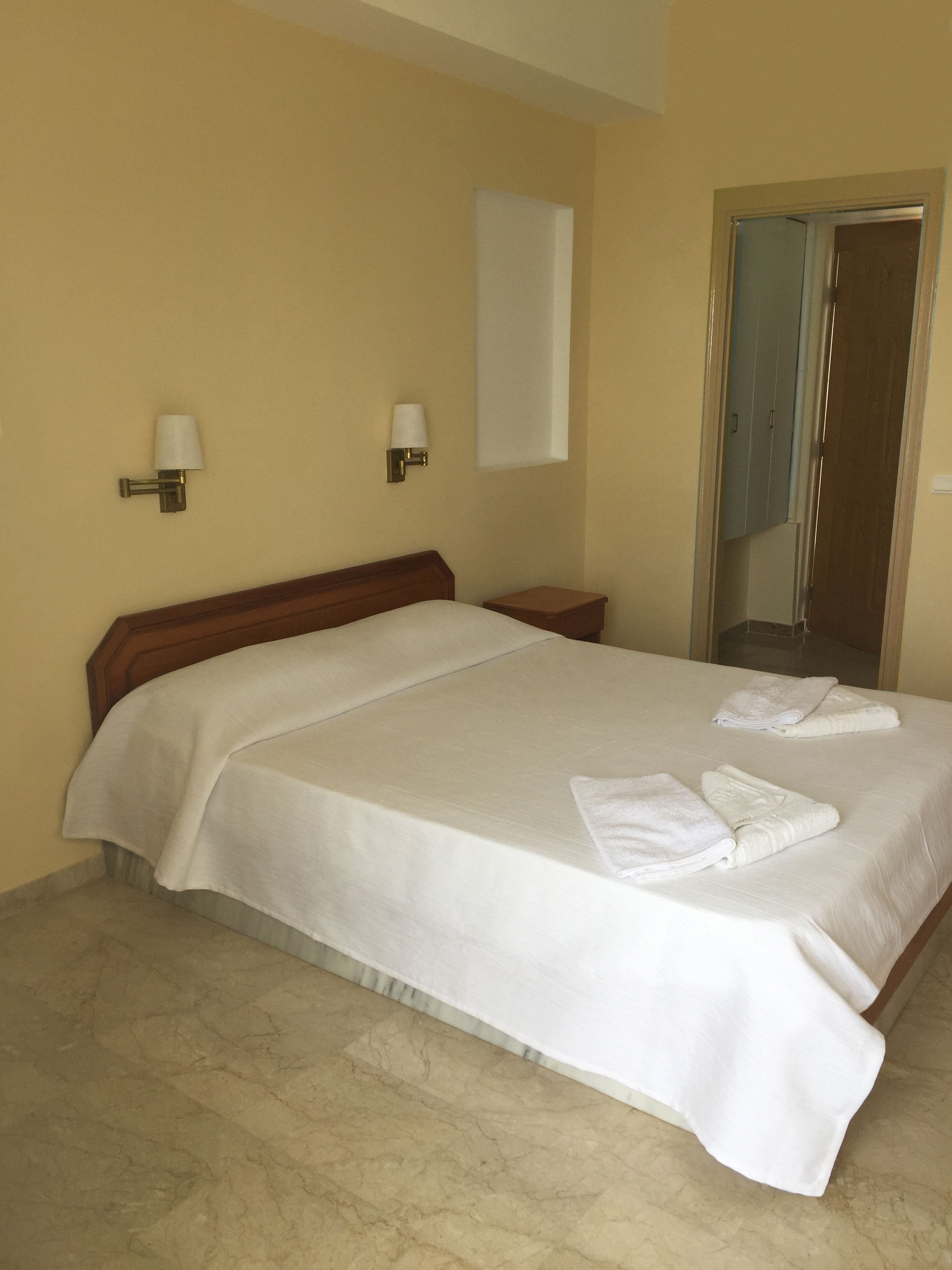 A hotel room with a large bed, two bedside lamps, a wooden headboard, a nightstand, and a mirror on the wall.