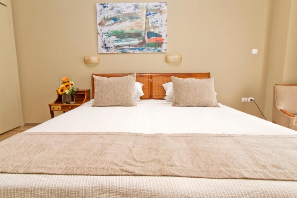 A hotel room with a large bed, two pillows, a nightstand with a vase of flowers, and a painting on the wall.
