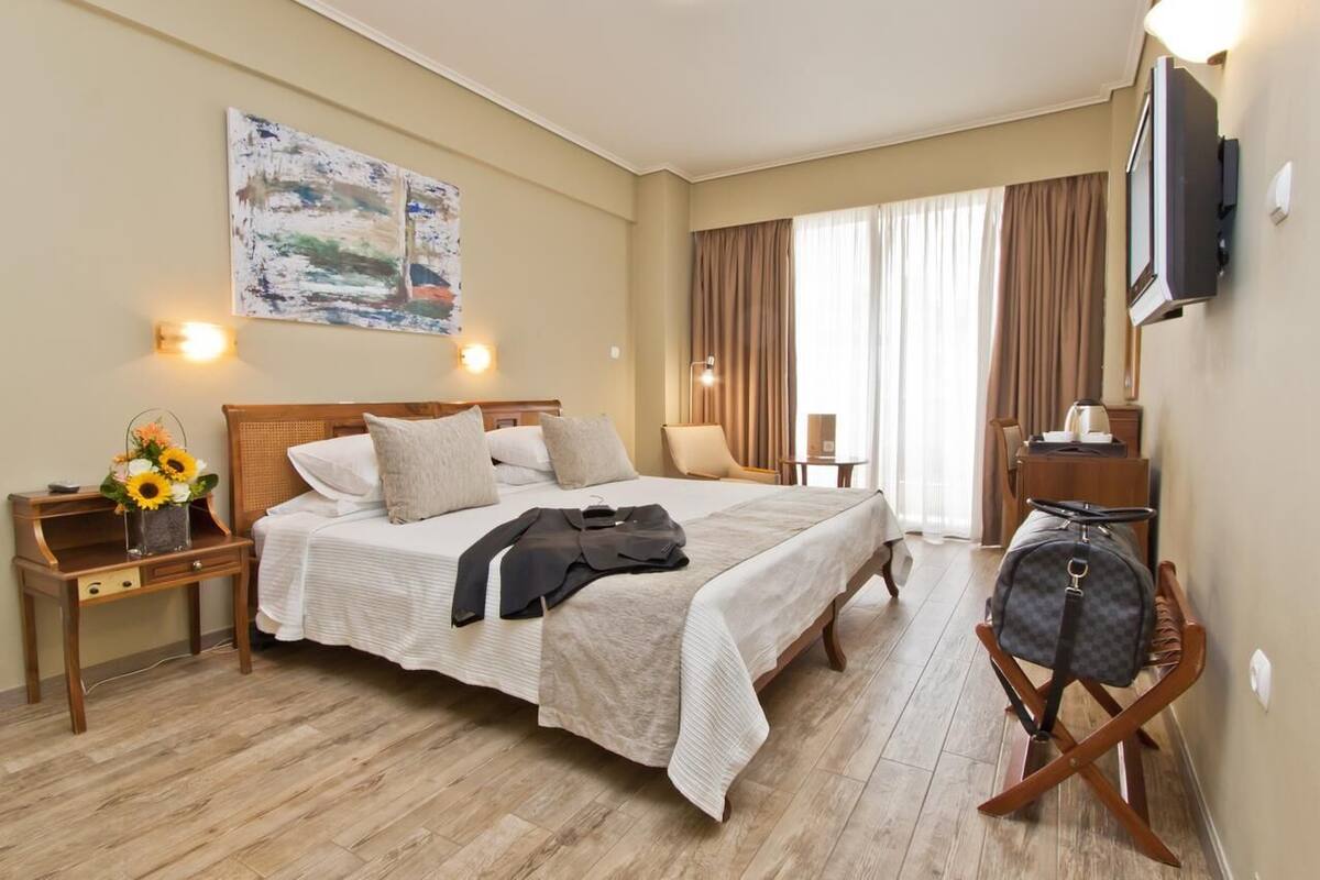 A hotel room with a large bed, a bedside table with a lamp, a TV mounted on the wall, and a suitcase on a chair.