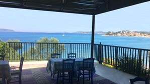 Un espace extérieur abrité, doté d’une table et de chaises, offrant une vue sur la côte, avec un ciel dégagé et une terre lointaine à l’horizon.