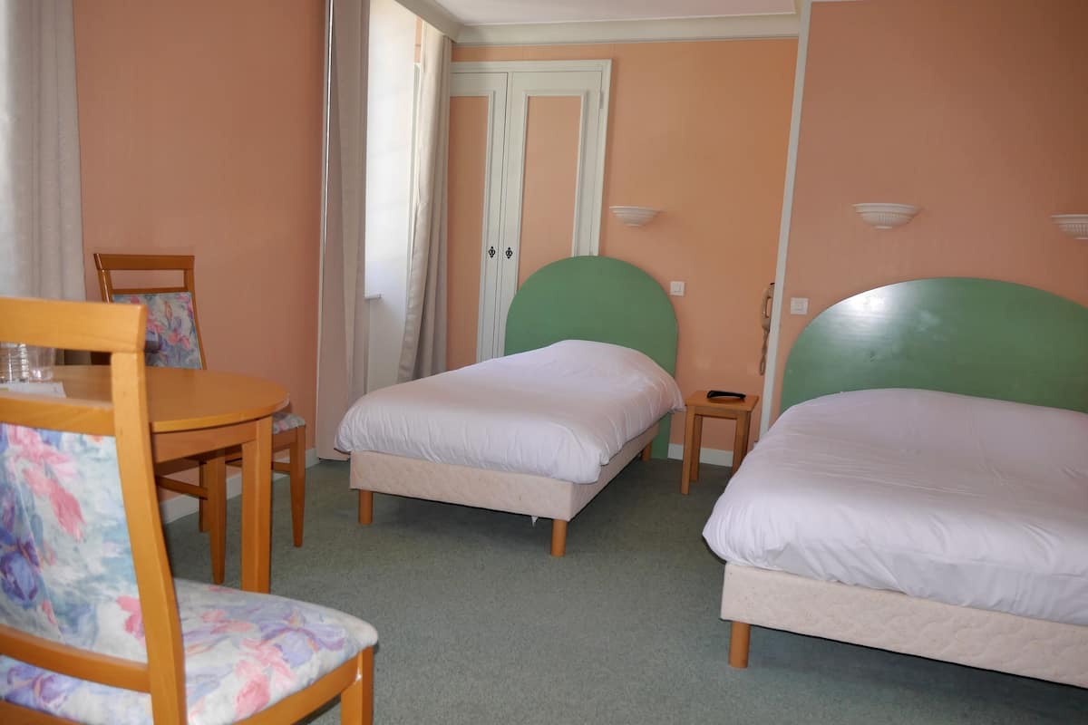 Une chambre d’hôtel avec deux lits simples, une petite table avec une chaise et une porte avec des rideaux.