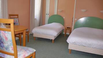 Una habitación de hotel con dos camas individuales, una pequeña mesa con una silla y una puerta con cortinas.