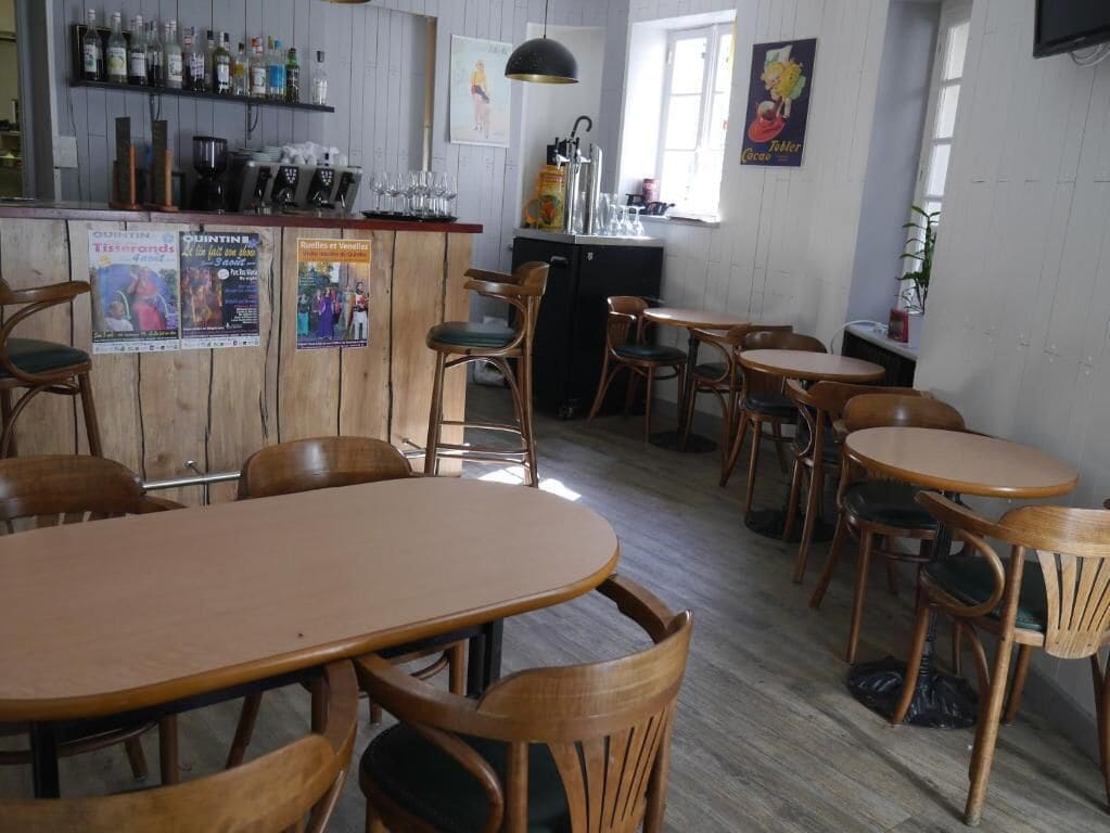 Eine gemütliche Bar mit Holztischen und -stühlen, einer Bar mit verschiedenen Flaschen sowie einem Plakat, das eine lokale Veranstaltung bewirbt.