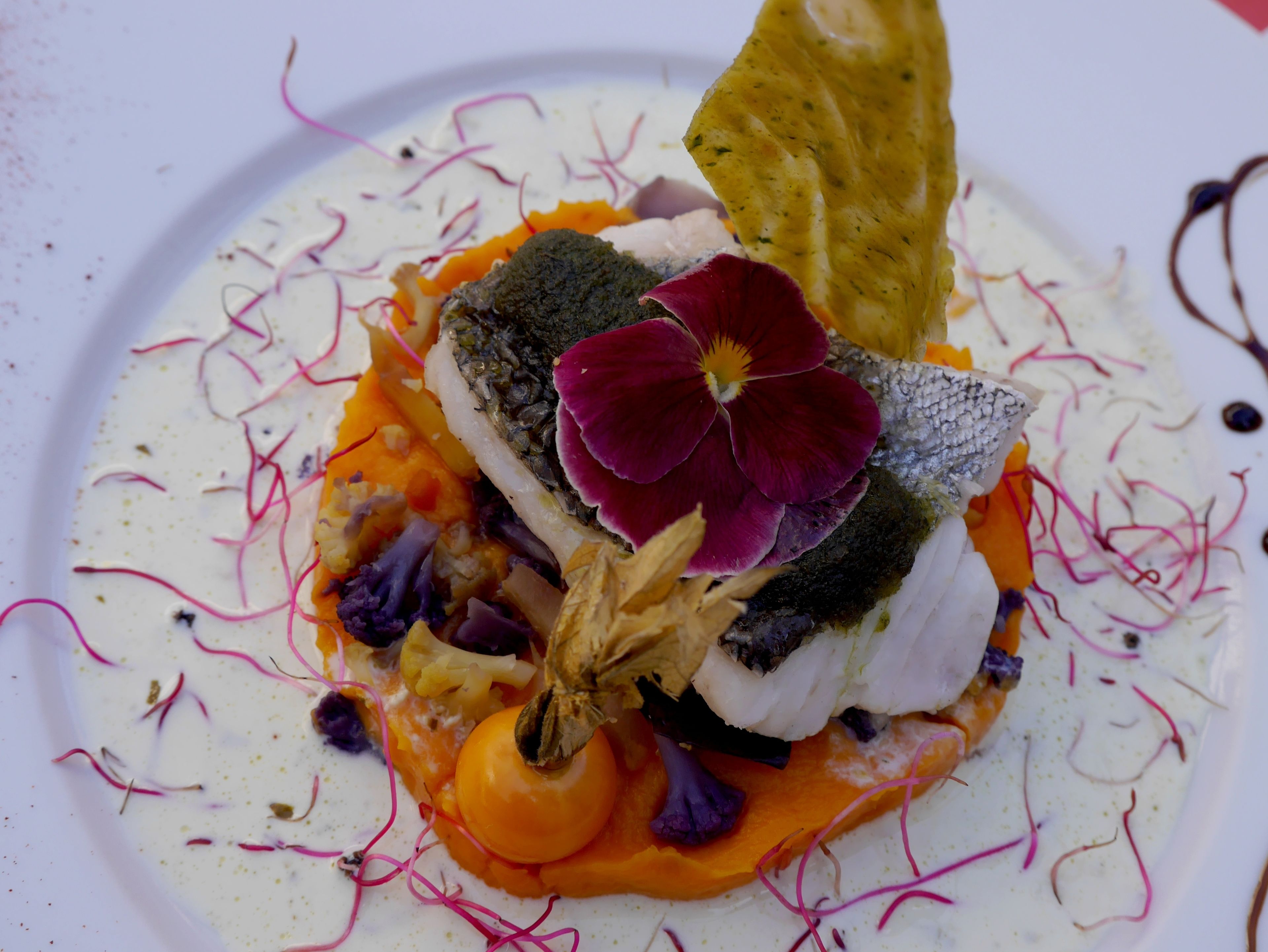 Une assiette avec un poisson, des légumes et une fleur.