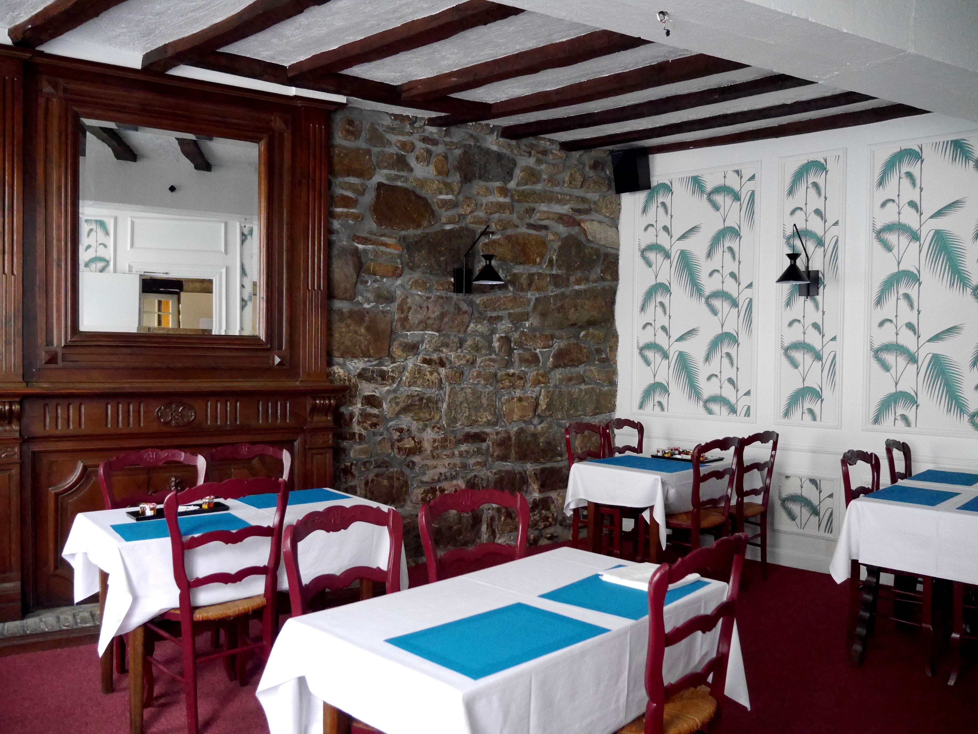 Un comedor con paredes de piedra, vigas de madera y sillas rojas. Las mesas están preparadas con manteles blancos y posavasos azules.