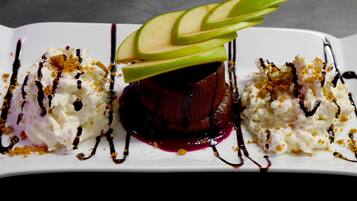 Um prato de sobremesa com um bolo vermelho escuro, fatias de maçã, chantilly e calda de chocolate.