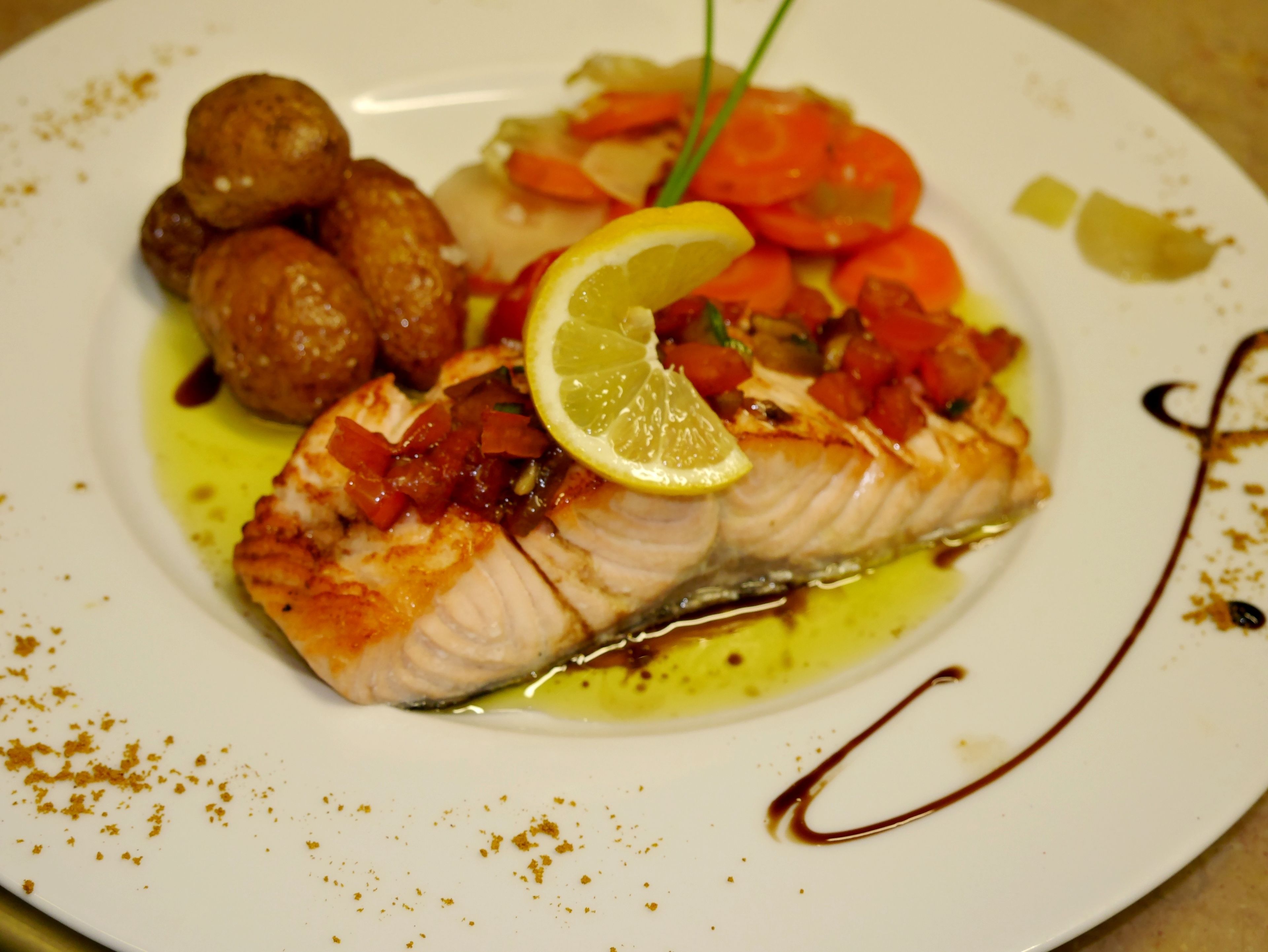 En tallrik med en bit fisk, grönsaker och en skiva citron.
