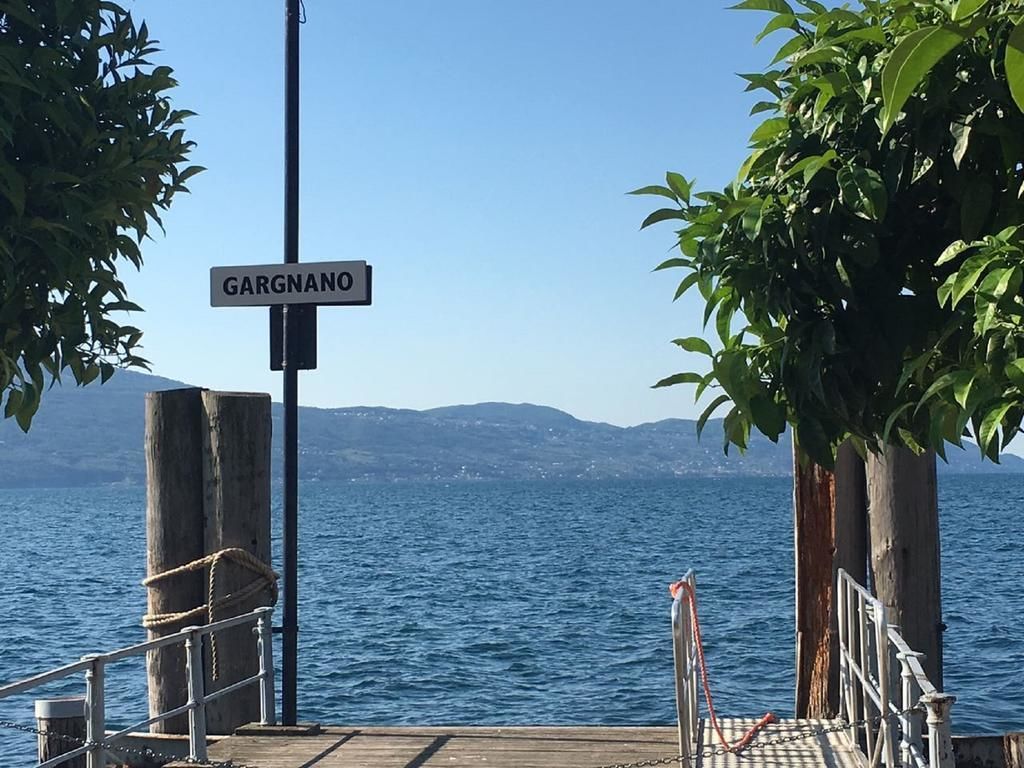 Ein Holzsteg mit einem Schild, auf dem 'GARGANO' steht, und Blick auf das Meer sowie ferne Berge.