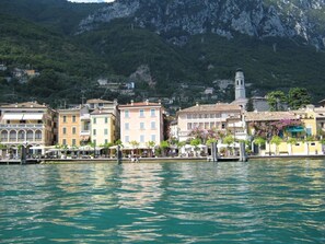 A waterfront town with buildings along the water, a prominent tower, and a mountainous backdrop.