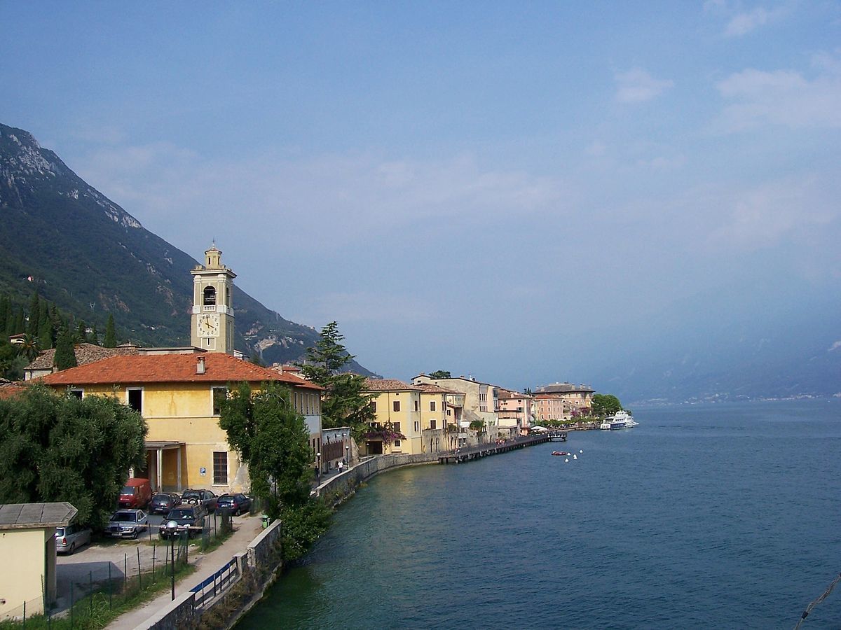A coastal town with a prominent church featuring a bell tower, a row of colorful buildings, and a calm sea.