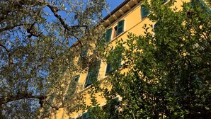 Un bâtiment à la façade jaune et aux volets verts, entouré d’arbres.