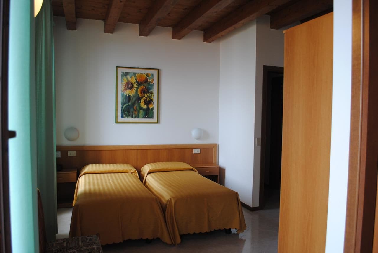 Ein Hotelzimmer mit zwei Betten, einem Holzkopfstück, einem Gemälde mit Sonnenblumen und einer Holztür.