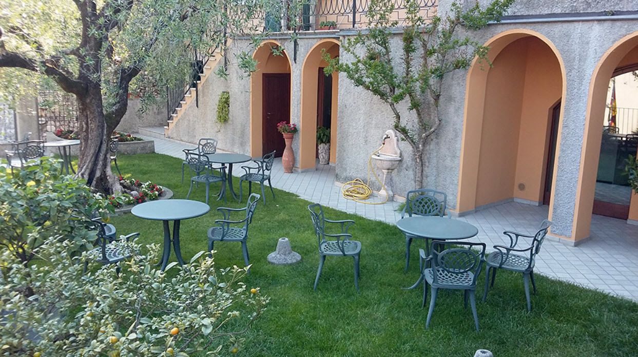 Une cour avec des sièges en plein air, un arbre et un bâtiment doté d’arcades.