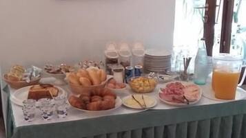 Un buffet de petit-déjeuner proposant une variété d’aliments et de boissons, un tableau encadré au mur et une fenêtre donnant sur un paysage verdoyant.