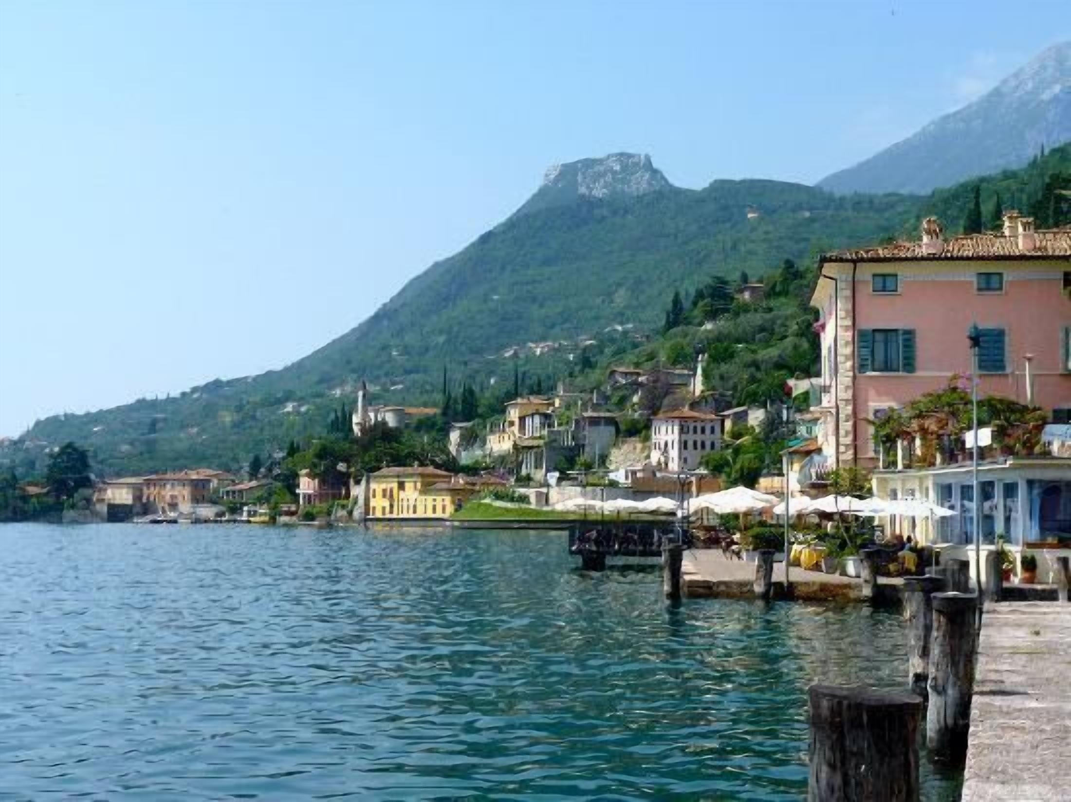 A lakeside town with buildings along the shore, a mountain in the background, and a dock extending into the water.