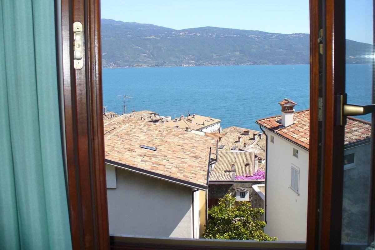 Vista des d'una finestra sobre una ciutat costanera, amb edificis i un mar blau clar.