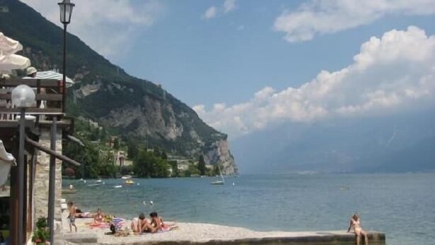 Un paysage côtier avec une falaise rocheuse, une plage où se trouvent des personnes et des bateaux sur l’eau.