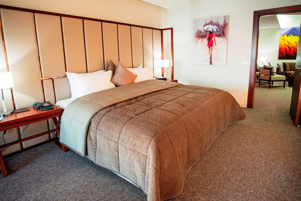 A hotel room with a large bed, a nightstand with a lamp, a chair, and a painting on the wall.