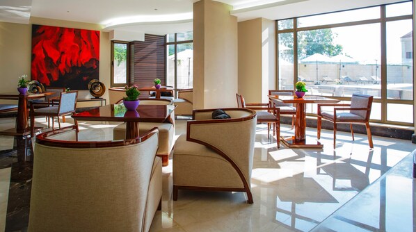 Un moderno vestíbulo de hotel con un ventanal grande, asientos cómodos y un cuadro abstracto rojo.