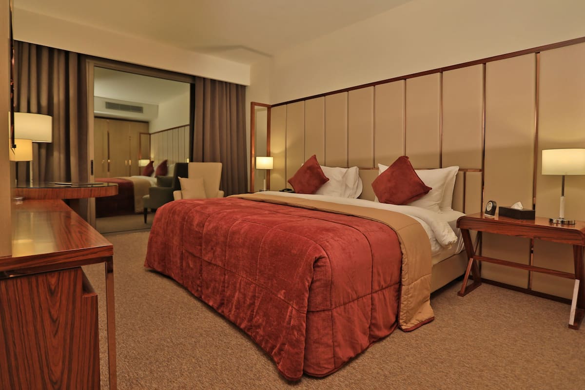 A hotel room with a large bed, a desk, a chair, a nightstand, and a mirror.
