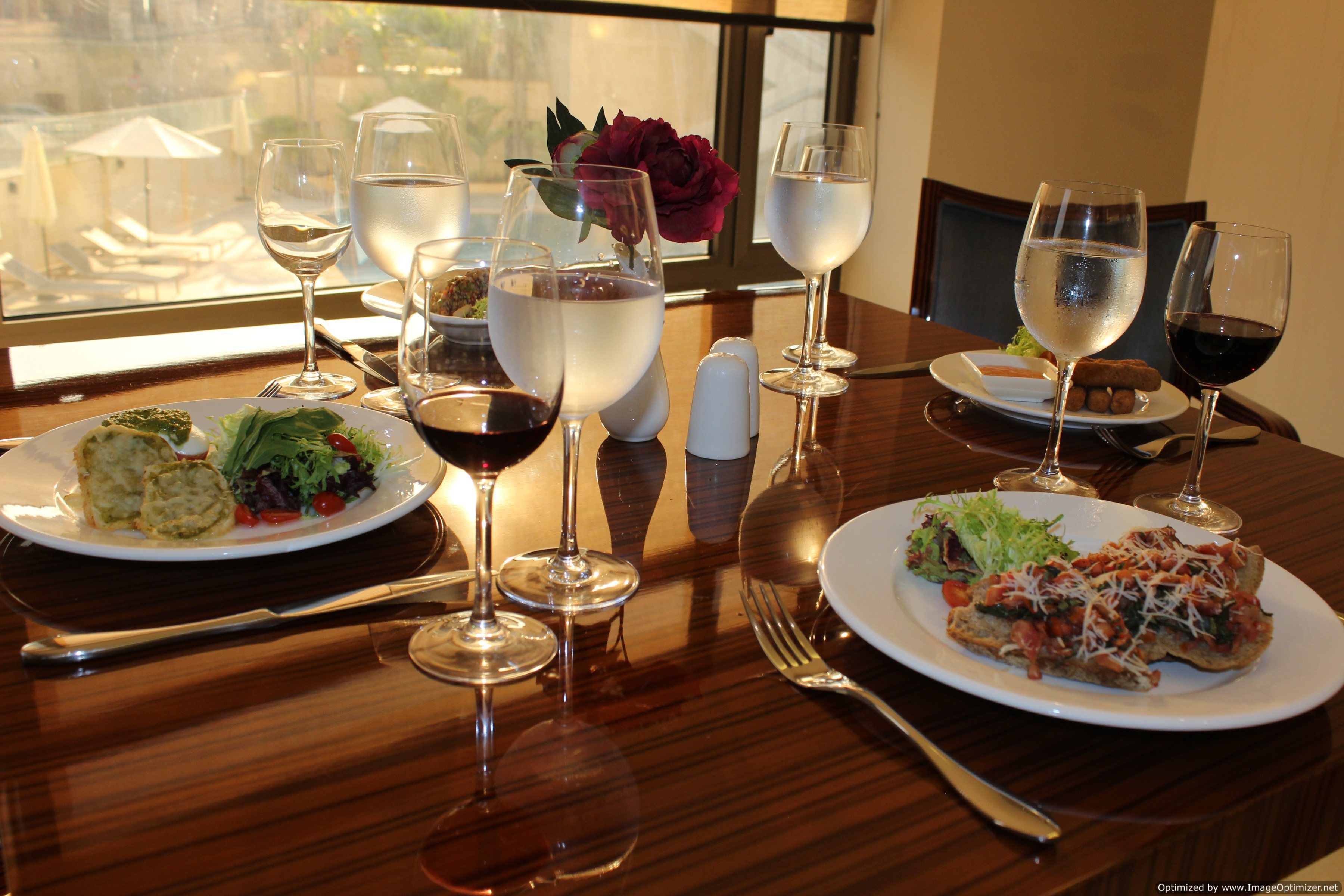 A dining table set with plates of food, wine glasses, and cutlery.