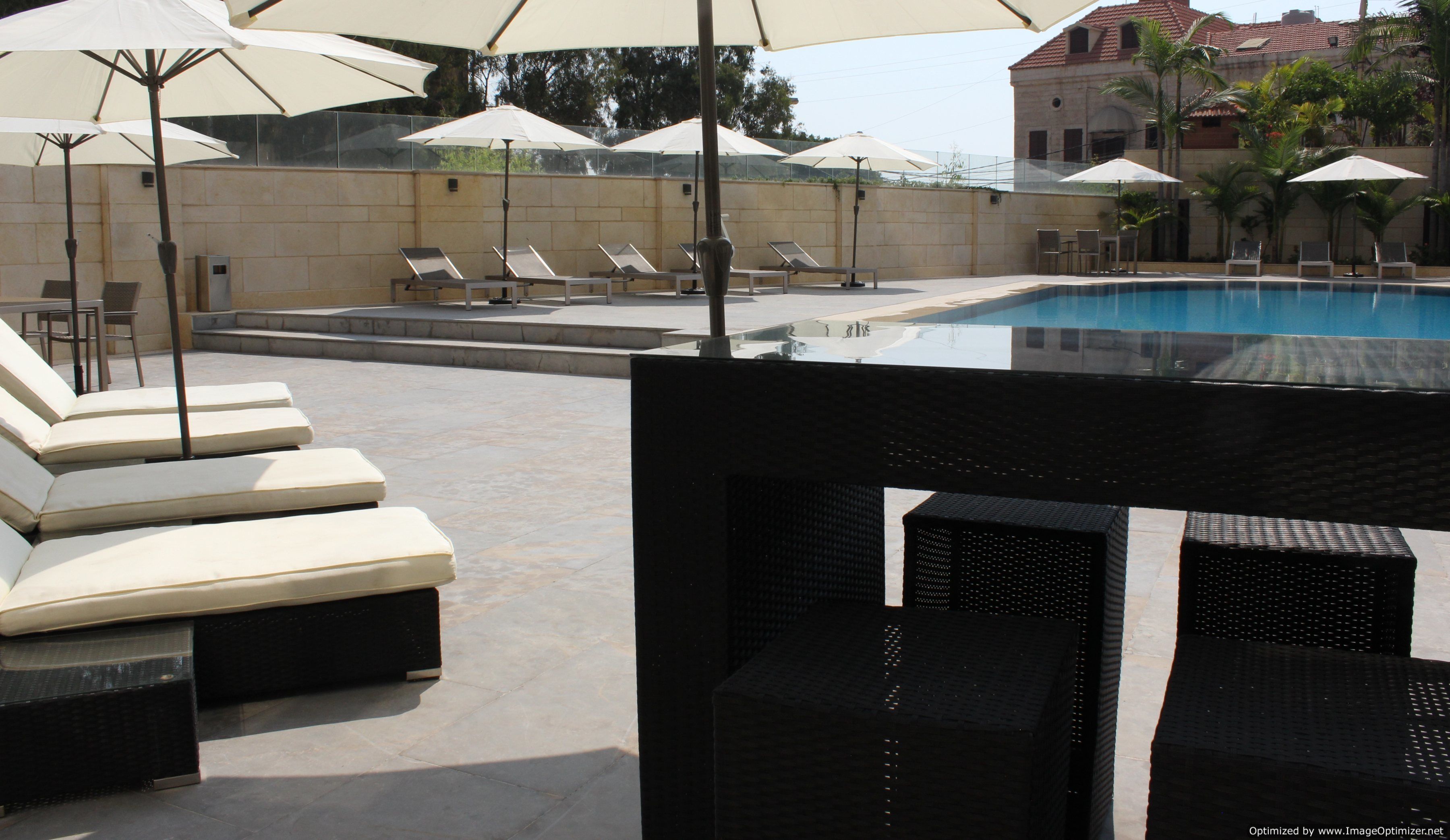 Ein Poolbereich mit Liegestühlen und Sonnenschirmen, mit freiem Blick auf den Pool und einem Gebäude im Hintergrund.
