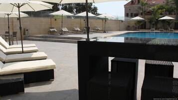 Ein Poolbereich mit Liegestühlen und Sonnenschirmen, mit freiem Blick auf den Pool und einem Gebäude im Hintergrund.