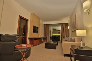 A hotel room with a sofa, a coffee table, a TV, a desk, and a lamp.