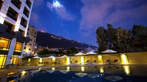 A nighttime pool area with lounge chairs and umbrellas, a clear sky, and a distant mountain view. - The Rooms Boutique Hotel (Jounieh)